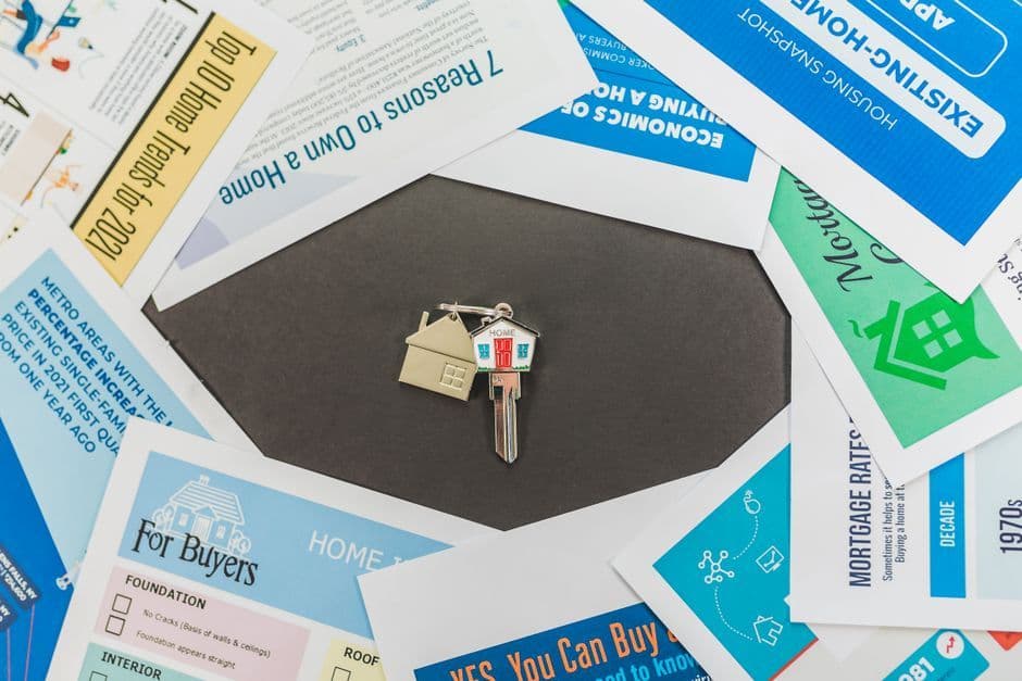 A house-shaped keychain and key resting on printed U.S. home-buying and mortgage-rate materials.