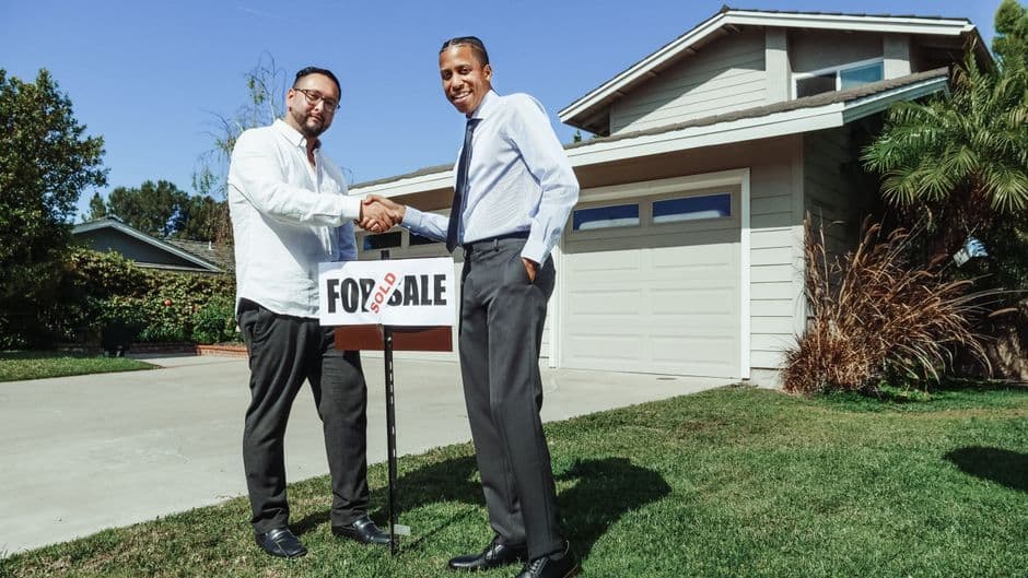 Two men shaking hands in front of a sold house, symbolizing a successful real estate transaction.
